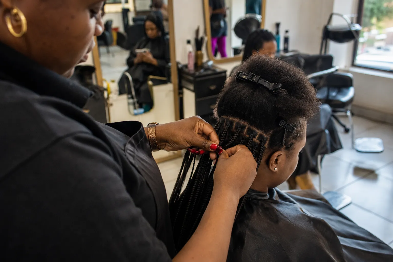 Professional hair stylist braiding a client's hair in a modern, brightly lit Kampalan beauty salon
